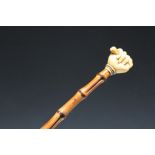 A GEORGIAN TYPE IVORY TOPPED BAMBOO WALKING CANE, the pommel in the form of a fist holding a bar,