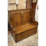 AN OAK CARVED SETTLE OF SMALL PROPORTIONS WITH LIFT-UP LID H-115 CM W-108 CM