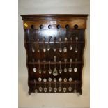 A COLLECTION OF SOUVENIR SPOONS MOUNTED ON AN OAK DISPLAY RACK
