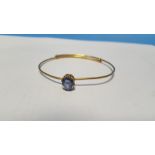 AN UNMARKED YELLOW METAL BANGLE SET WITH POSSIBLY A SAPPHIRE. Approx. weight 8.9 g