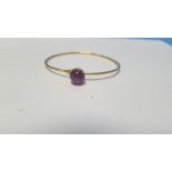 AN UNMARKED YELLOW METAL BANGLE SET WITH A PURPLE CABACHON POSSIBLY AMETHYST. Approx. weight 7.8 g