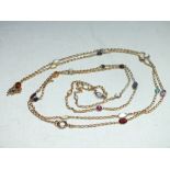 AN UNMARKED YELLOW METAL FLAPPER LENGTH CHAIN SET WITH POLISHED AND FACETED SEMI-PRECIOUS GEMSTONES,