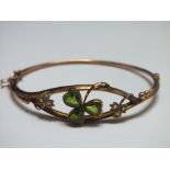 A 9CT GOLD SHAMROCK BANGLE, set with green peridot type stones with two further seed pearl set