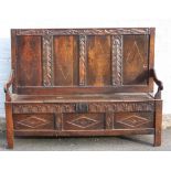 AN ANTIQUE OAK AND INLAID PANELLED SETTLE, the four panel high back with carved decoration and