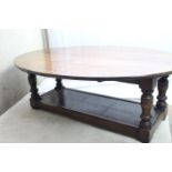An oval dropleaf solid wood low/coffee table with turned uprights and solid lower tier shelf, length