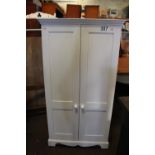 Modern small white wardrobe. Two panelled doors with porcelain knobs and single hanging rail.