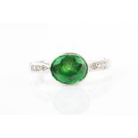 A platinum, diamond, and tsavorite garnet ring collet-set with a mixed oval-cut garnet, the