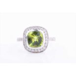 An 18ct white gold, diamond and peridot ringcentred with a faceted cushion-cut peridot, within a