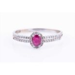 A diamond and ruby halo cluster ringcentred with an oval-cut ruby within a border of diamonds, the