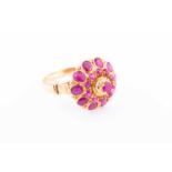 A yellow metal and ruby cluster ring, set with a raised cluster of round-cut rubies, shank