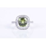 An 18ct white gold, diamond and peridot ring, centred with a faceted cushion-cut peridot, within a