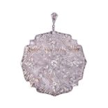 A diamond pendant / brooch of rounded openwork design, centred with a round brilliant-cut diamond of