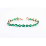 A yellow metal and emerald line bracelet, set with twenty-one mixed oval-cut emeralds, approximately