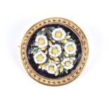 A yellow metal and micro mosaic brooch, of rounded form, depicting daisies against a black