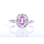 A platinum, diamond, and pink sapphire cluster ring, set with an emerald-cut pink sapphire of