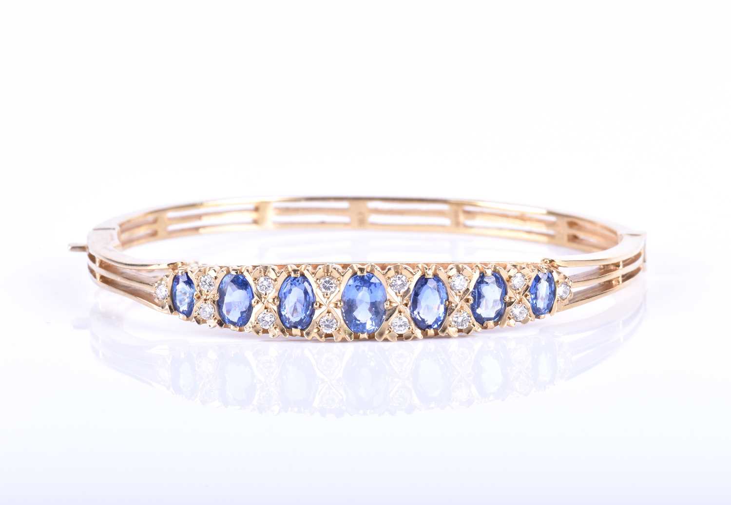 A 9ct yellow gold, diamond and sapphire bangle, set with seven graduated mixed oval cut blue