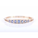 A 9ct yellow gold, diamond and sapphire bangle, set with seven graduated mixed oval cut blue