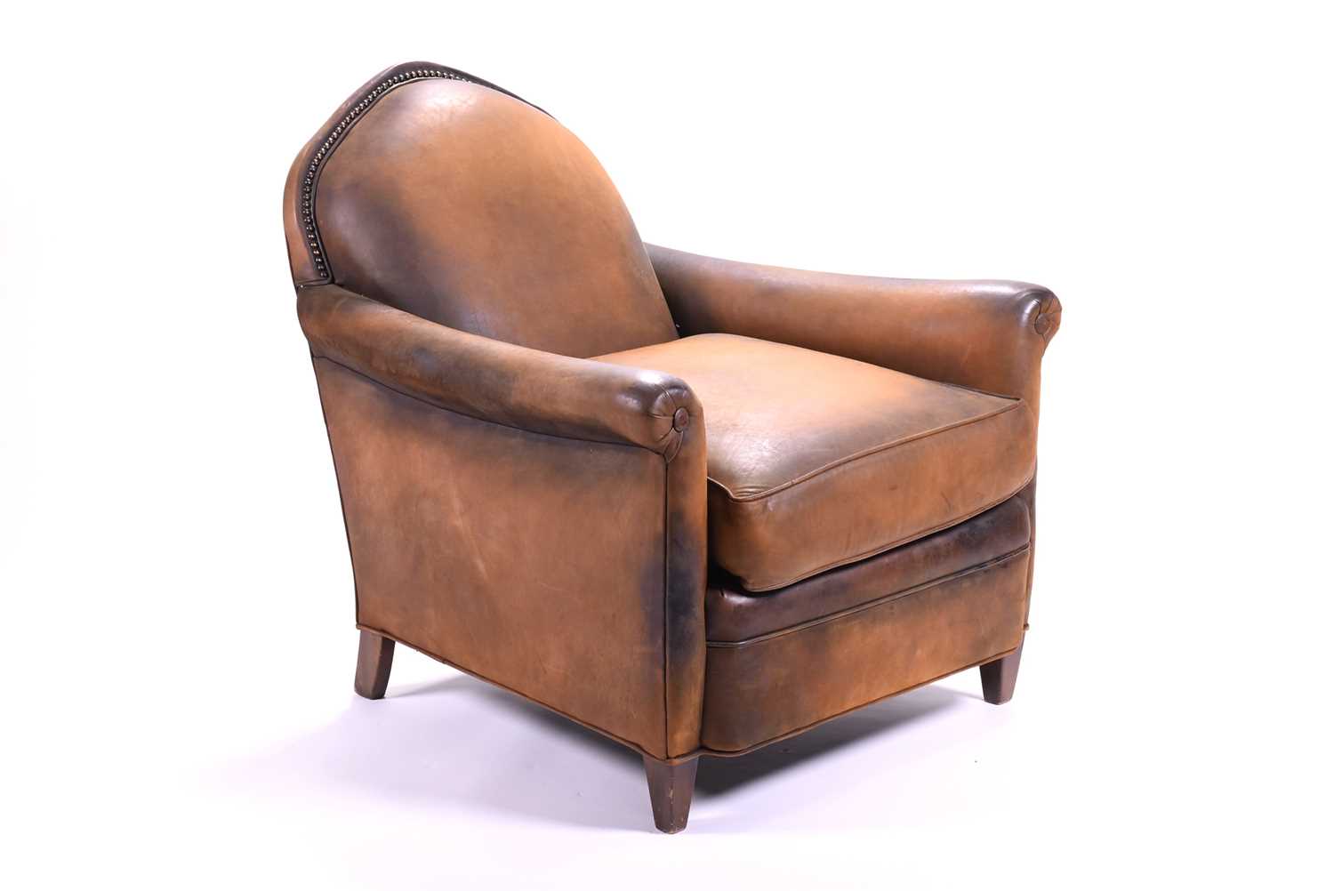 A tan leather club armchair with padded seat and curved armrests, with loose fitted cushion and