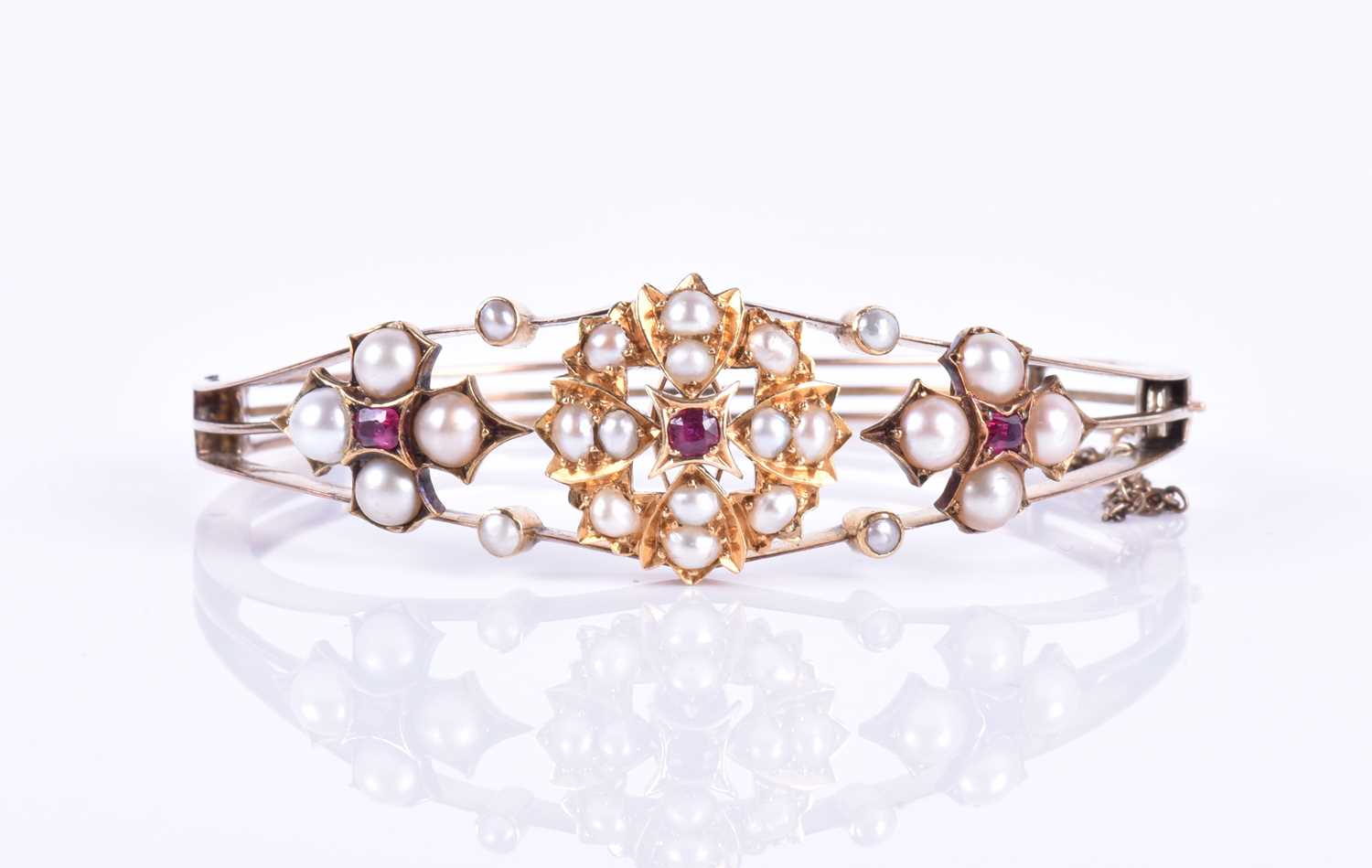 A Victorian 15ct yellow gold, pearl, and ruby banglethe hinged mount centred with a bright cut