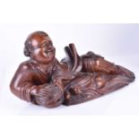 A Chinese carved wooden model of a reclining child smiling and holding a wicker basket, a bat
