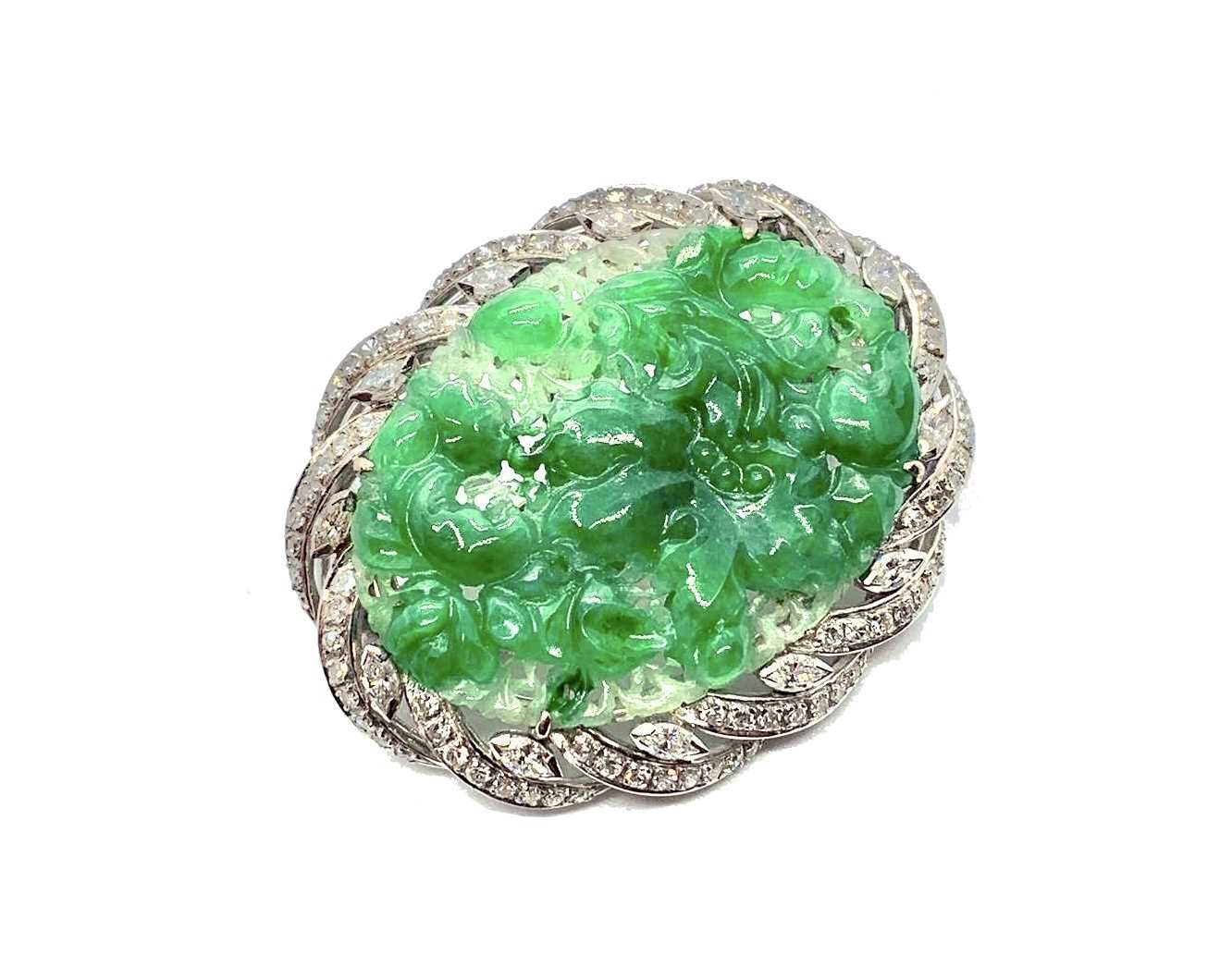 An 18ct white gold jade and diamond brooch, the central piece of carved jade surrounded by diamonds.