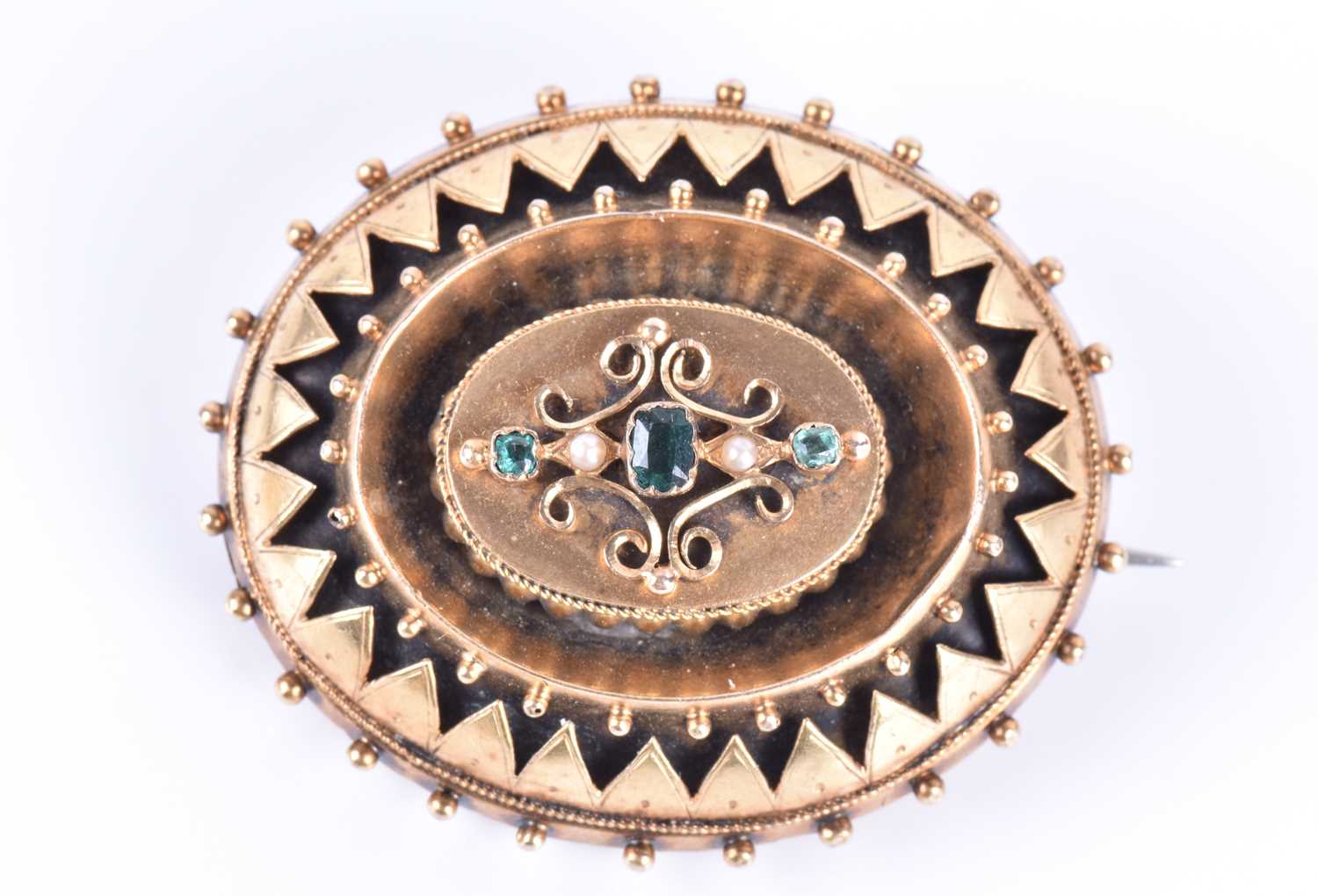 A Victorian Etruscan Revival yellow metal, emerald, and pearl broochof oval form, centred with three