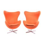 A pair of 1970s Arne Jacobsen style Egg chairs, upholstered in orange fabric, and supported on metal