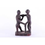 An unusual carved hardwood Tribal figure of standing holding each other, one with a stick, supported