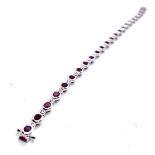 An 18ct white gold ruby and diamond bracelet. 23 rubover set oval rubies of good colour weighing a