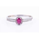 A diamond and ruby halo cluster ring, centred with an oval-cut ruby within a border of diamonds, the