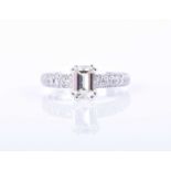 An 18ct white gold and diamond ringcentered with a four-claw set emerald-cut diamond of