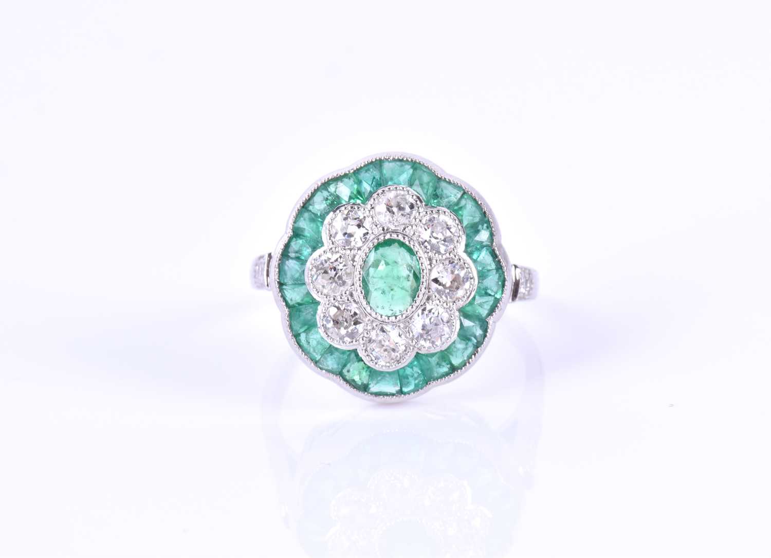 A diamond and emerald cocktail ringcentred with a mixed oval-cut emerald, within a border of round