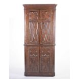 An early 20th century oak floor-standing corner cupboard in two sections, with shaped carved doors