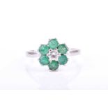 An 18ct white gold, diamond, and emerald daisy cluster ringcentred with a round brilliant-cut