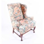 A Georgian style mahogany wing armchair, upholstered in floral fabric, with scrolled arms, and