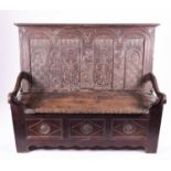A 19th century oak settle, probably Welsh, with carved decoration to the back depicting masks and