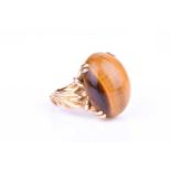 A 9ct yellow gold and tigers eye ring set with an oval cabochon tigers eye, with swept design to