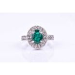 A diamond and emerald cluster ring, set with a mixed oval-cut emerald within a border of round