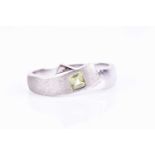 A white metal and peridot crossover ring, the smooth and matte mount inset with a square-cut