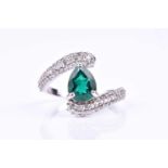 A diamond and emerald crossover style ring, set with a pear-shaped emerald, within a border of round