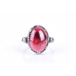 An unusual diamond and garnet ring, set with an oval cabochon garnet, set in a silver mount, flanked
