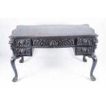 A large Victorian style carved and stained oak desk, the serpentine top over a central frieze drawer