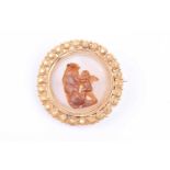 A yellow metal and onyx hardstone cameo brooch, of circular form, depicting a cherub climbing rocks,