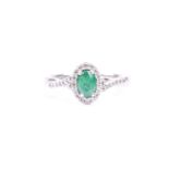 A platinum, diamond, and emerald cluster ring, set with a mixed oval-cut emerald, within a border of