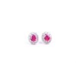 A pair of white gold, diamond, and ruby cluster earrings, set with two oval-cut rubies (
