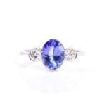 A platinum, diamond, and tanzanite ring, bezel-set with a mixed oval-cut tanzanite of