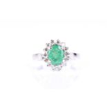 An emerald and diamond cluster ring, the oval cut emerald, in four claw mount within a border of