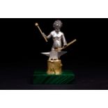 An Italian silver and silver-gilt figure of a cherubis blacksmith at the anvil, on malachite base,