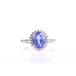 A tanzanite and diamond cluster ring, the oval cut sapphire claw mounted wihin a border of round