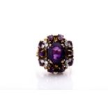 A diamond and amethyst cluster cocktail ring, the raised mount set with an oval-cut amethyst